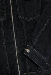 Mörk denimjacka med dragkedjestängning, två bröstfickor och kontrasterande sömmar. Inkluderar knapppyntade ärmslut och vadderad inredning.