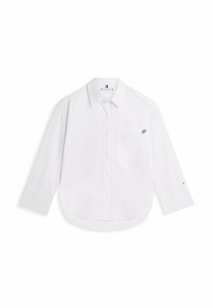 Camisa blanca de manga larga con botones, un bolsillo en el pecho y un pequeño logotipo bordado en el bolsillo y en el puño de la manga izquierda.