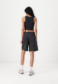Zwarte cropped tanktop gecombineerd met hoge zwarte denim shorts. Het model draagt lichtroze sneakers en witte crew sokken.