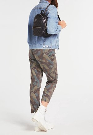 Denimjakke, sort quilted mini rygsæk, camouflerede bukser i grønne og brune nuancer, og hvide ankelstøvler med chunky såler.