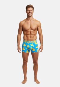 Herren blaue Boxershorts mit einem sich wiederholenden Muster von gelben Gummienten. Elastischer Bund mit dem gelben Text "MUR UKKO".
