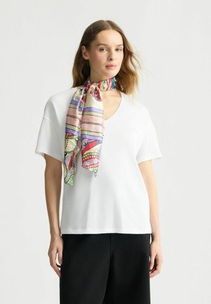 T-shirt bianco a V abbinato a una sciarpa di seta a fantasia colorata legata attorno al collo. L'outfit è completato da pantaloni scuri.