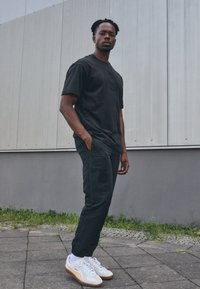 Čierne bavlnené tričko s jemneembosovaným logom, skombinované s čiernymi športovými nohavicami so bočnými vreckami a vyšitými akcentmi. Biele tenisky.