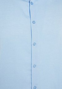 Světle modrá, texturovaná košile na knoflíky s přední légou se šesti odpovídajícími knoflíky. Látka má jemný vzor.