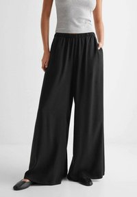 Pantaloni largi negri, cu talie elastică, realizați dintr-un material moale și ușor, având buzunare laterale și un design fluid.