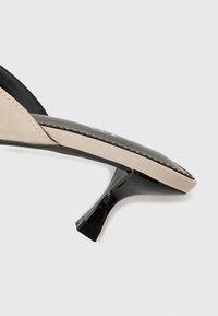 Čierna a béžová slingback topánka na podpätku s špicatou špičkou. Lesklý povrch, úzky podpätok a kontrastné farebné panely. Minimalistický dizajn.