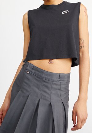 Osoba nosząca czarny, bezrękawnikowy crop top Nike oraz szarą plisowaną spódnicę z wysokim stanem, z piercingiem w pępku i tatuażami na rękach.