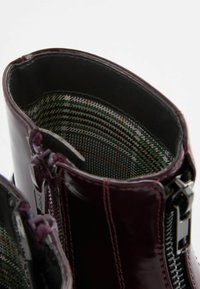 Bottine en cuir verni bordeaux à finition lisse, dotée d'une doublure textile à motifs et d'une fermeture éclair latérale avec quincaillerie métallique.