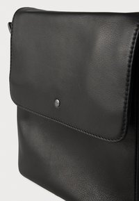 Μαύρη δερμάτινη τσάντα με λεία υφή, σχεδίαση με καπάκι και μεταλλικό κούμπωμα. Ραφές κατά μήκος των άκρων.