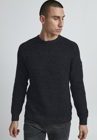 Maglione a maglia grigio scuro con un motivo testurizzato, collo a giro, maniche lunghe e un piccolo dettaglio del logo sulla manica sinistra.