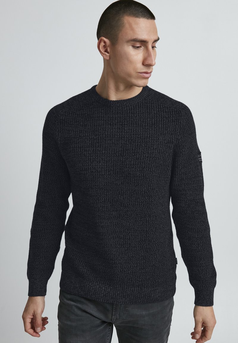 Maglione a maglia grigio scuro con un motivo testurizzato, collo a giro, maniche lunghe e un piccolo dettaglio del logo sulla manica sinistra.