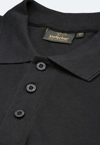 Schwarzes Polo-Shirt aus strukturiertem Stoff, mit einer Knopfleiste mit drei Knöpfen in dunkler Farbe und einem Kragen. Das Etikett enthält den Markennamen.