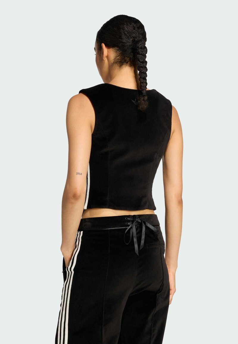 Zwarte cropped mouwloze top van zachte stof, met een gladde textuur en strakke lijnen. Gecombineerd met zwarte broek en een strikdetail in de taille.