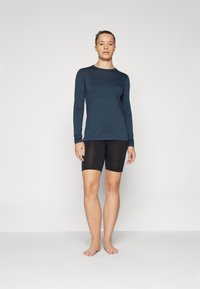 Dark blue long-sleeve shirt with a round neckline, worn with black knee-length shorts. Fabric appears smooth and fitted.