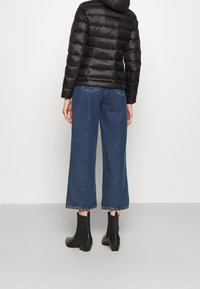 Sort pufferjakke med hætte, parret med brede blå denimjeans med frynset kant og sorte ankelstøvler.