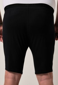 Shorts en coton noir avec une texture lisse et une taille élastique, présentant un motif logo subtil le long du bord supérieur.