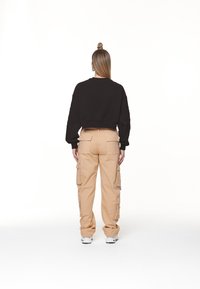 Schwarzer, verkürzter Sweatshirt und beige Cargo-Hosen mit mehreren Seitentaschen, in lässigem Schnitt und mit gerippten Bündchen, kombiniert mit weißen Sneakers.