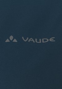 Mörkblått tyg med en slät textur som har en ljusgrå "Vaude"-logotyp och en triangelikon. Enkel, ren design.