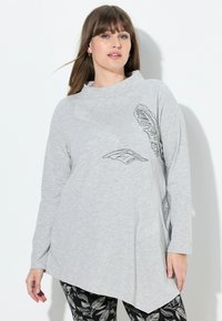 Helles graues Langarmoberteil mit schwarzer Blattstickerei, hohem Kragen und asymmetrischem Saum. Glatte, weiche Stofftextur.