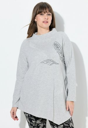 Helles graues Langarmoberteil mit schwarzer Blattstickerei, hohem Kragen und asymmetrischem Saum. Glatte, weiche Stofftextur.