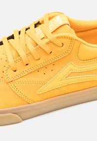Sárga velúr sneaker, textúrált felső résszel, sima sárga bőr logó akcentussal és lapos fűzőkkel. Szellőzés érdekében perforációkkal rendelkezik.