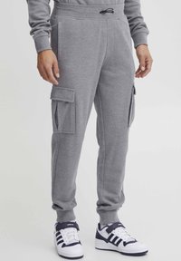 Gray fleece joggers with side cargo pockets, elastic cuffs, and drawstring waist. Paired with white and navy sneakers.