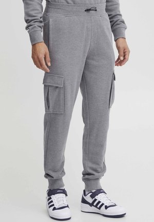 Gray fleece joggers with side cargo pockets, elastic cuffs, and drawstring waist. Paired with white and navy sneakers.