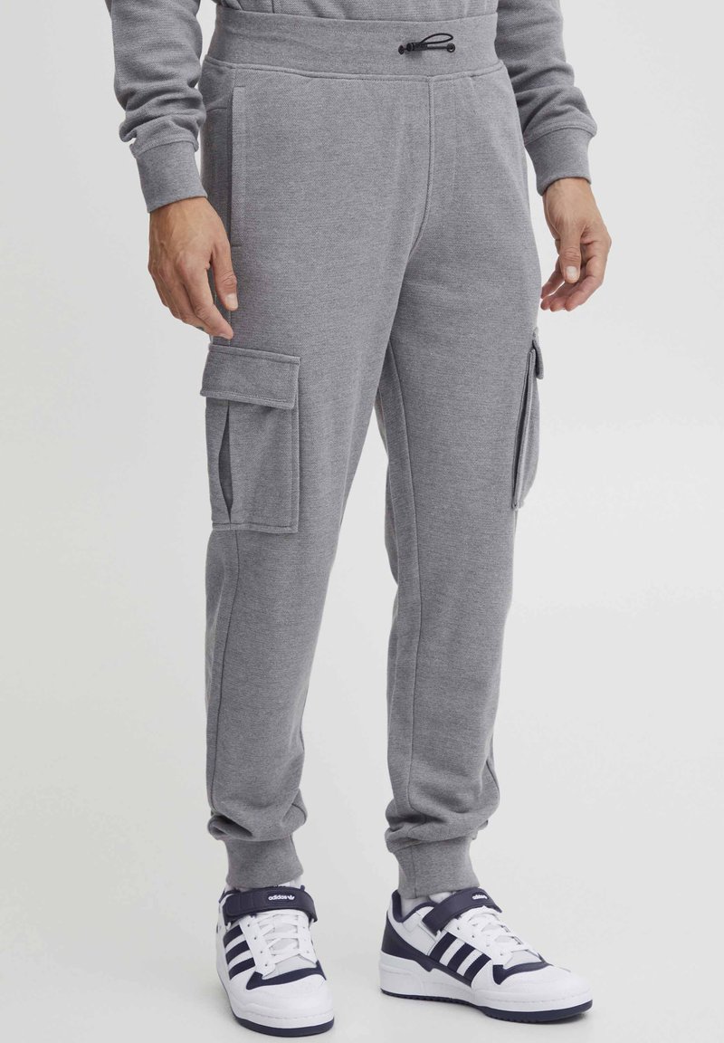 Gray fleece joggers with side cargo pockets, elastic cuffs, and drawstring waist. Paired with white and navy sneakers.