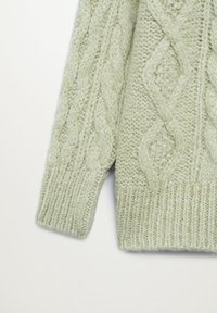 Manche et partie du torse d'un pull tricoté vert clair avec détails en motif torsadé et diamant, poignets et ourlet côtelés sur fond blanc.