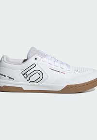 Scarpa sportiva bianca con tomaia testurizzata, perforazioni, dettagli neri e suola in gomma naturale. Presenta un marchio in evidenza sul lato.