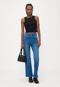 Crna bezrukavna majica, plave široke traperice i crna torba s zakovicama. Glatka tekstura, ležeran kroj, s jednostavnim metalnim detaljima.