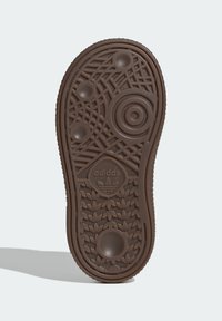 Brown rubber sneaker sole with textured patterns, circular designs, and an embossed logo in the center, featuring raised accents and grooves.