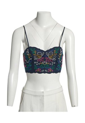 Marineblaues Crop-Top mit dünnen Trägern und symmetrischer, mehrfarbiger Blumenstickerei auf einem weißen Schaufenster-Torso, der weiße Hosen trägt.