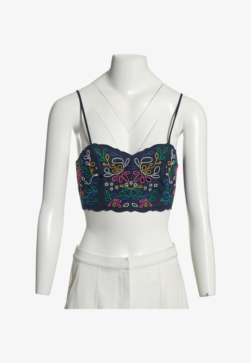 Haut court bleu marine à fines bretelles avec une broderie florale multicolore symétrique sur un buste de mannequin blanc portant un pantalon blanc.