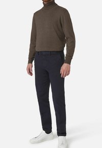 Bruine coltrui, slim-fit marineblauwe broek en witte sneakers. De trui heeft een ribbelstructuur; de broek is glad met een klassieke snit.