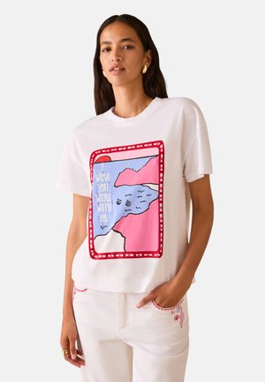 Donna che indossa una maglietta bianca con una grafica rossa, rosa e blu che mostra il mare, il sole e la scritta "Vorrei che fossi con me."