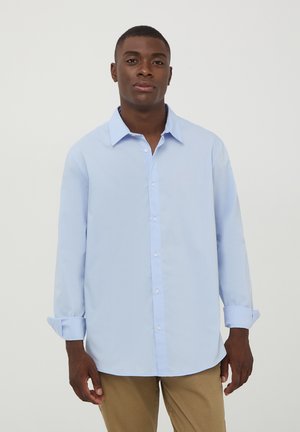 Camicia azzurra chiara con colletto, maniche lunghe e polsini arrotolati. Realizzata in un tessuto liscio con un design classico.