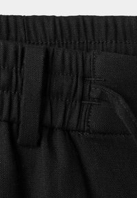 Gros plan d'un tissu noir montrant une taille élastique avec des coutures et une passants de ceinture sur un vêtement.