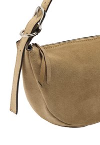 Beżowa torebka typu crossbody z zamszu o zaokrąglonym kształcie, z suwakiem oraz płaskim paskiem z metalowym pierścieniem w kolorze srebrnym do regulacji.