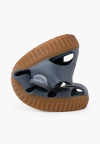 Sandales en caoutchouc grises avec une semelle marron à motifs, présentant des côtés ouverts et une forme arrondie. Détails notables incluant des sections découpées et des accents texturés.