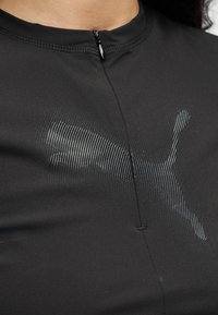 Κοντινό πλάνο μαύρου τοπ με ένα διακριτικό υφασμάτινο λογότυπο Puma στο στήθος και ένα μικρό φερμουάρ στο ντεκολτέ.