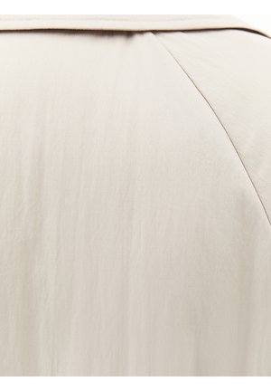 Primer plano de tela beige que muestra un material liso y ligero con costura a lo largo de una costura diagonal.