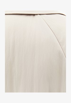 Primer plano de tela beige que muestra un material liso y ligero con costura a lo largo de una costura diagonal.