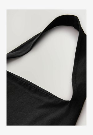 Bolsa de mano de algodón negro con una correa ancha y plana y una textura suave; presenta un diseño simple y una superficie sin adornos.