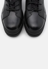 Chaussures en cuir noir à finition lisse, bout arrondi et lacets proéminents, avec une semelle texturée pour une meilleure adhérence.