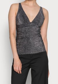 Top noir pailleté à col en V plongeant et côtés froncés, fabriqué dans un matériau extensible, associé à un pantalon noir.