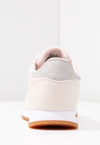 Ljusrosa sneakers med en slät läderöverdel, silverglitterdetalj vid hälen, vit mellansula och en beige gummisula.