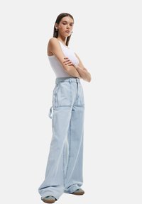 Ljusblå vida denimbyxor med framfickor, hög midja, bälteshällor och en avslappnad passform, i kombination med en vit linne.