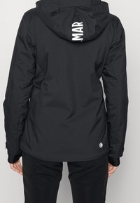 Rückansicht einer Person in einer schwarzen Jacke mit Kapuze, die teilweise weißen Text "MAR" auf der Kapuze und ein kleines rundes Logo nahe dem Saum zeigt.