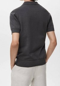 Polo à manches courtes gris foncé avec col et poignets côtelés, texture lisse et coupe ajustée, porté avec un pantalon de couleur claire.